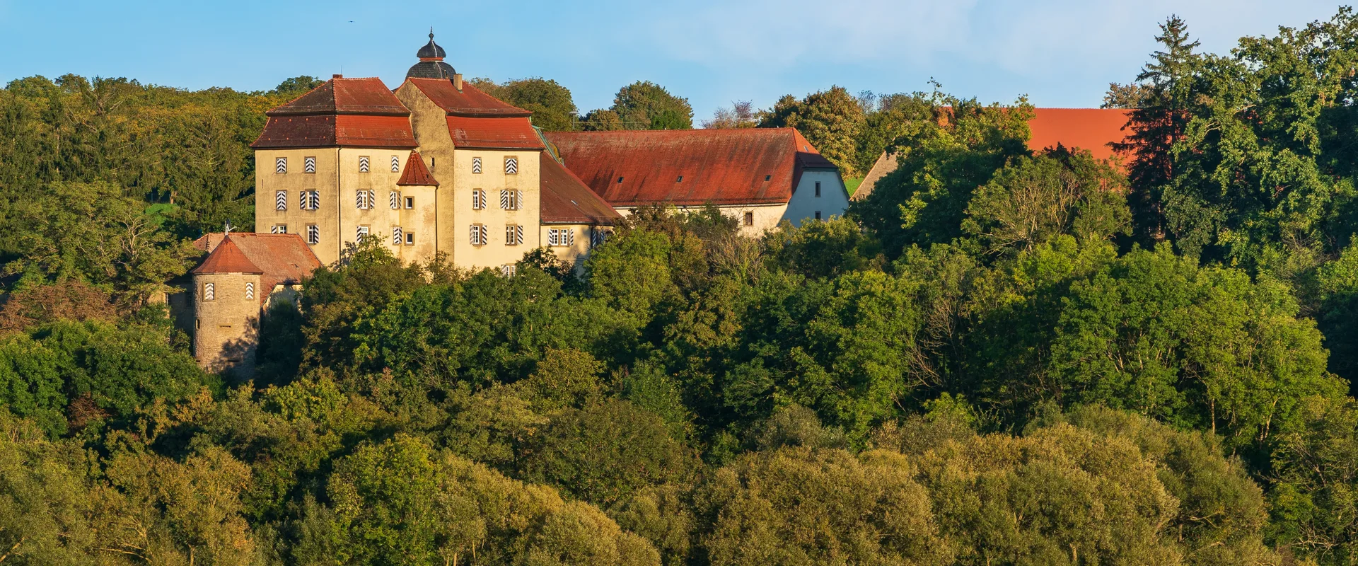 Schloss Heuchlingen im Bad Friedrichshaller Stadtteil Duttenberg über einem bewaldeten Hang im Abendlicht